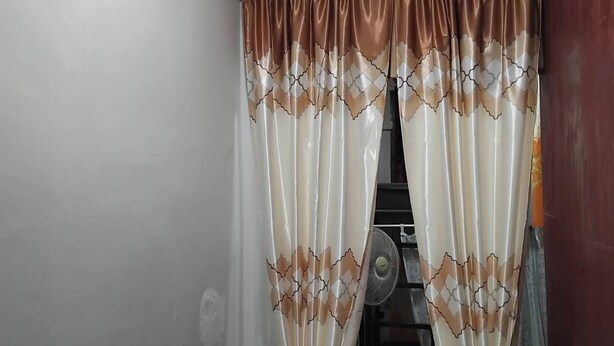 Ein Badezimmer mit weißer Wand, einem Ventilator und einem Vorhang mit geometrischem Muster.