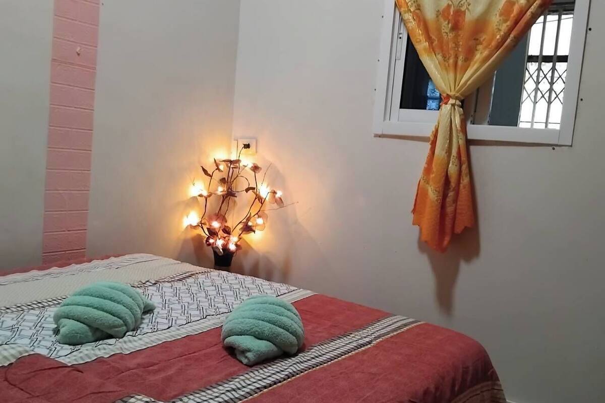 A bedroom with a bed, a wall-mounted light, and a window with curtains.