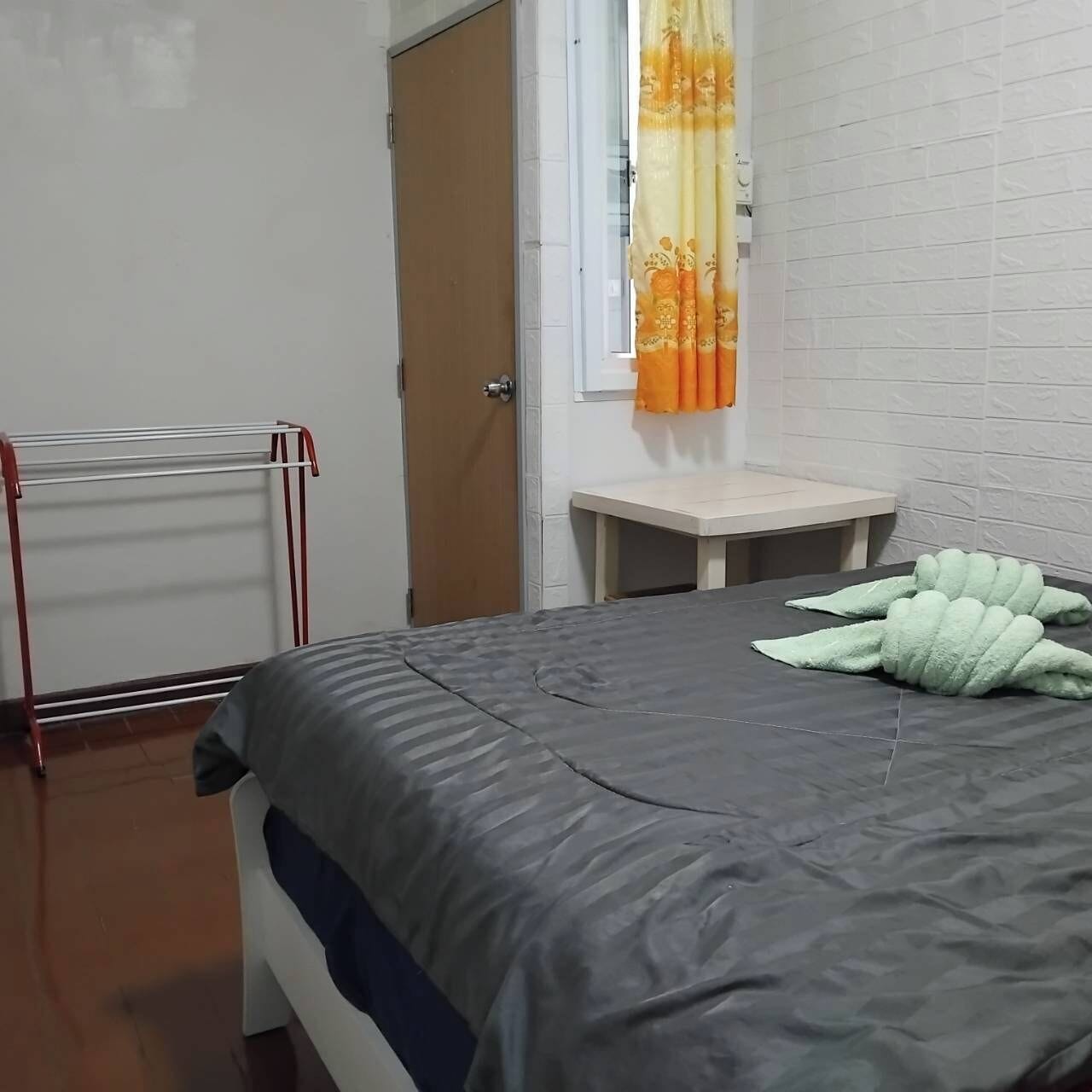 A bedroom with a bed, a small table, a drying rack, and a window with curtains.
