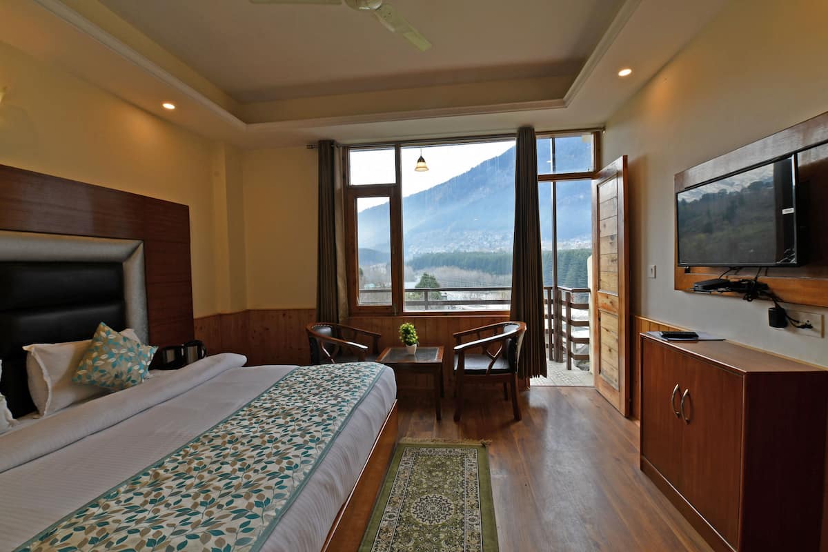 A hotel room with a bed, a desk, a chair, a television, and a view of mountains through large windows.