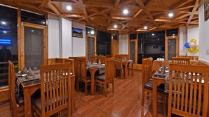 A restaurant with wooden ceiling beams, tiled floors, and wooden chairs and tables. - Lotus Inn Rothang View (Manali)