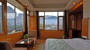 A room with a bed, a chair, a table, and a view of mountains. - Lotus Inn Rothang View (Manali)