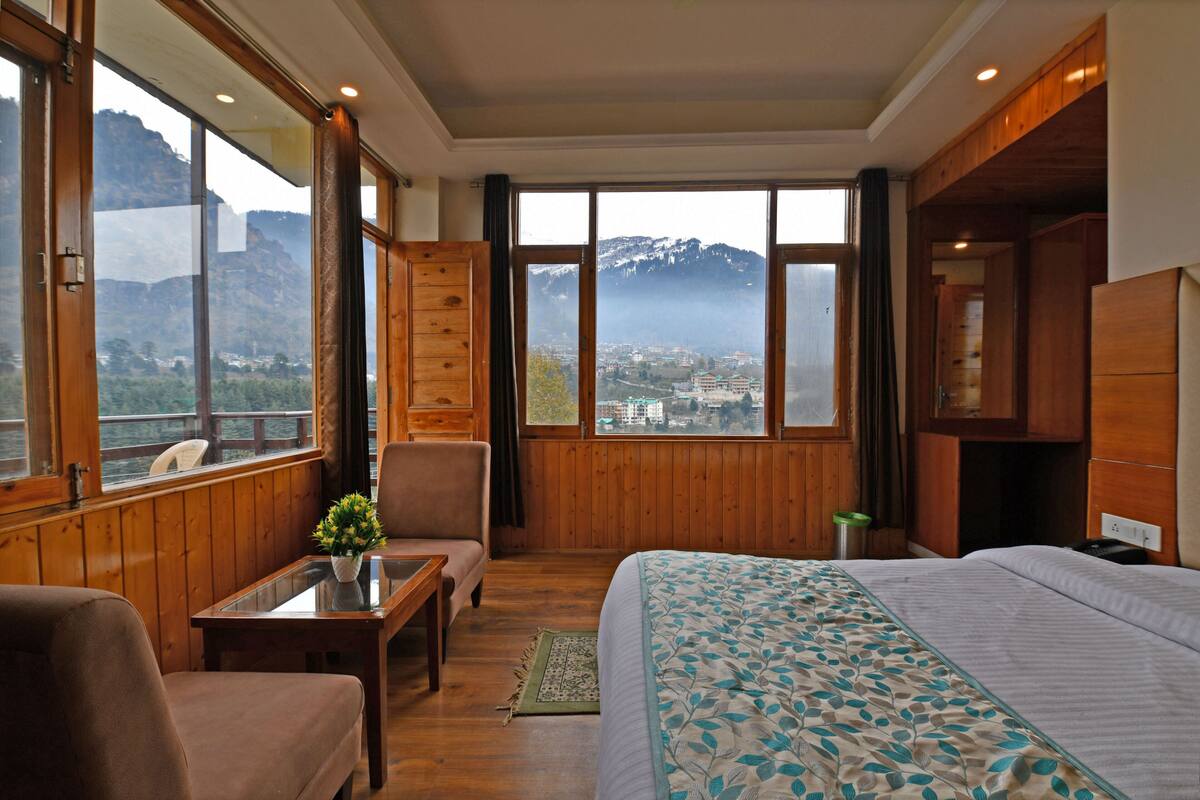 A room with a bed, a chair, a table, and a view of mountains.