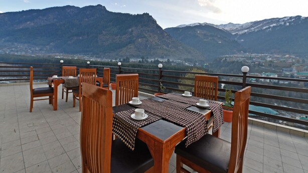 A terrace with tables and chairs, overlooking a mountainous landscape. - Lotus Inn Rothang View (Manali)