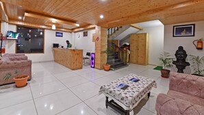 A lobby with a wooden ceiling, a reception desk, a staircase, and a sofa. - Lotus Inn Rothang View (Manali)