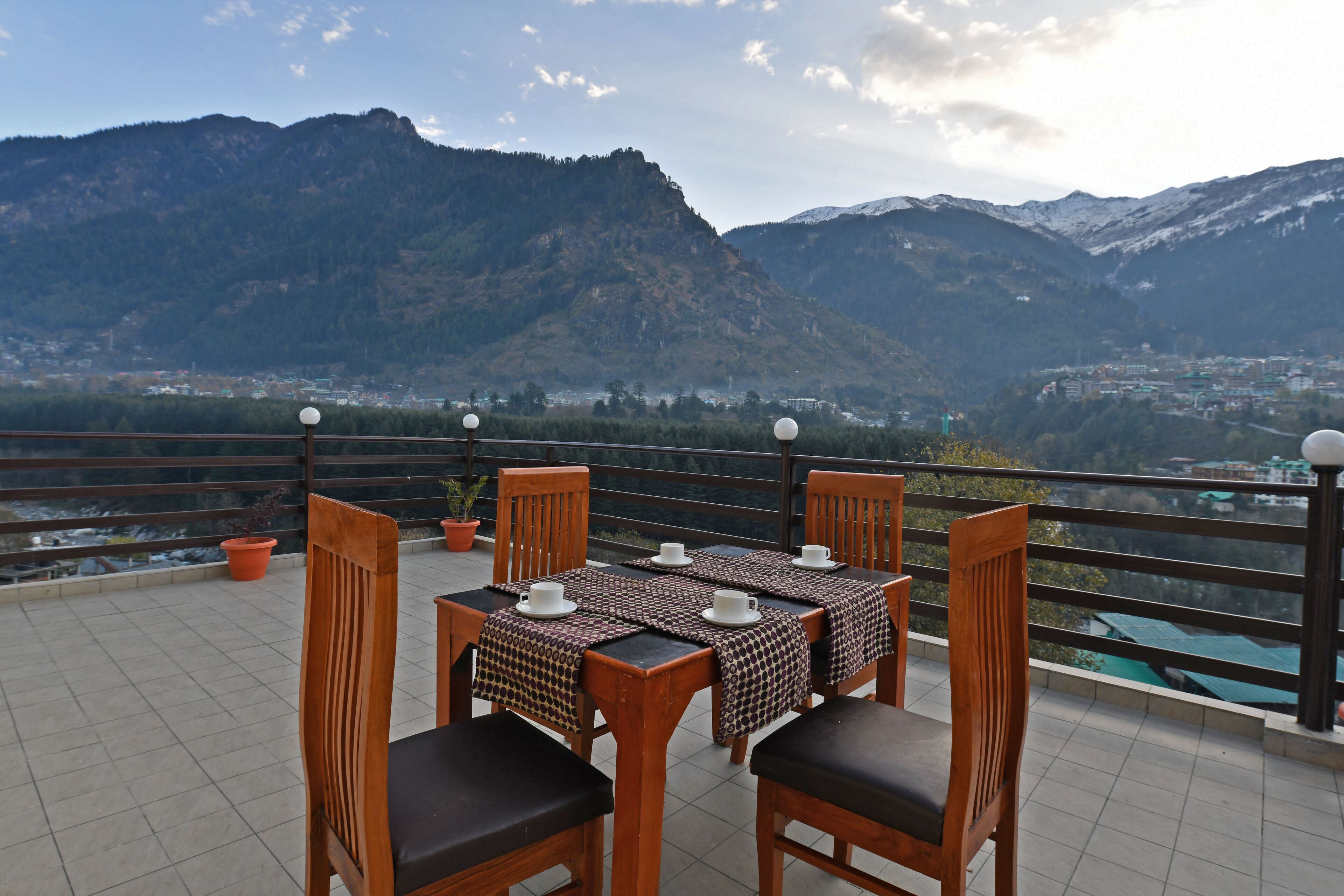 A terrace with a table set for four, overlooking a mountainous landscape.