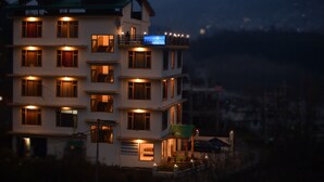 A multi-story hotel with illuminated windows and balconies, a visible sign, and a green roof. - Lotus Inn Rothang View (Manali)