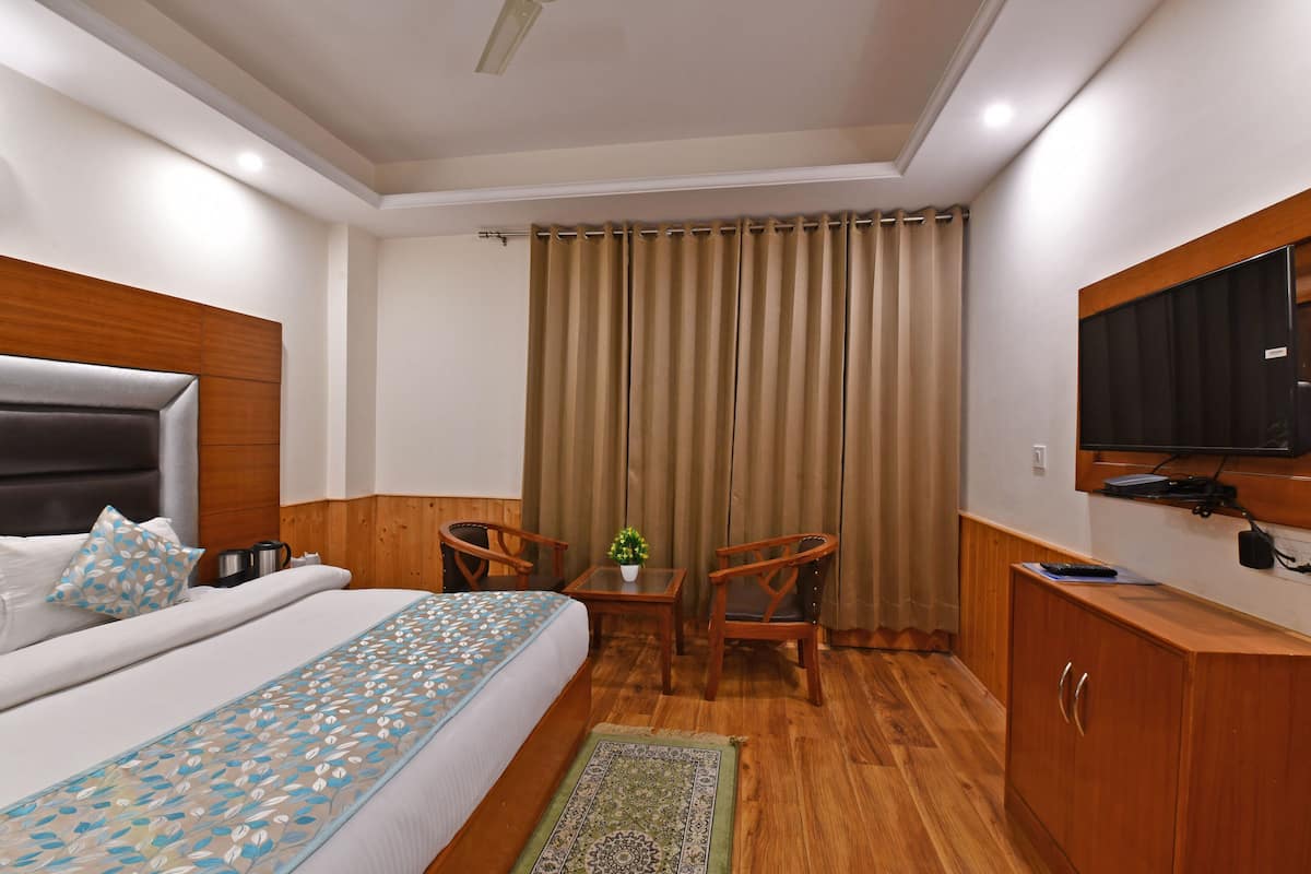 A hotel room with a bed, a desk, two chairs, a television, and a wardrobe.