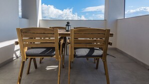 A balcony with a wooden table and chairs, a lantern, and a view of the sky. - Apartments Pejakovic (Vir)