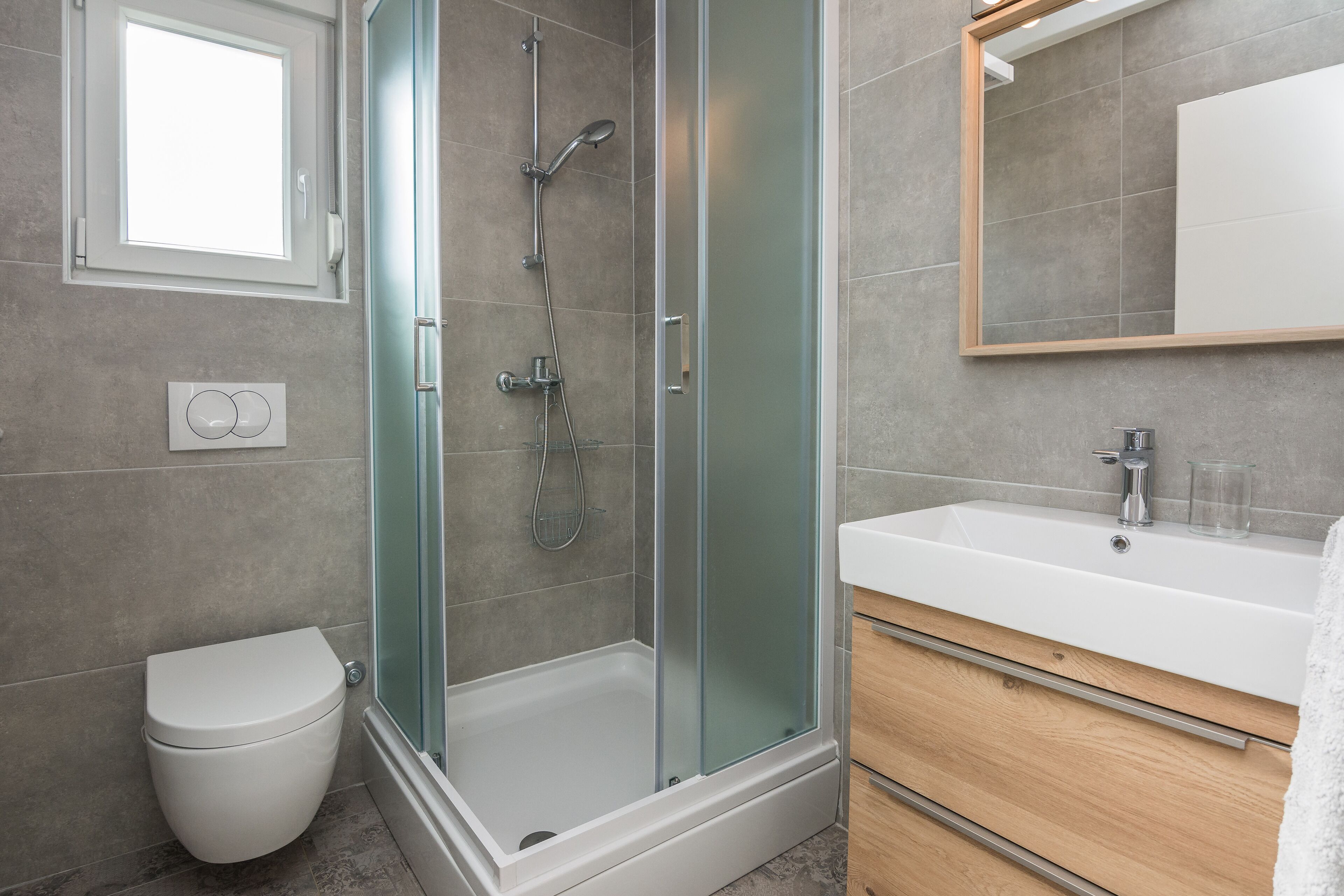 Un baño moderno con ducha envuelta en vidrio, inodoro blanco y tocador de madera con espejo.