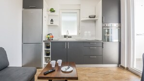 A compact kitchen with a refrigerator, oven, and sink. There is a dining table with cups and a remote control. - Apartments Pejakovic (Vir)