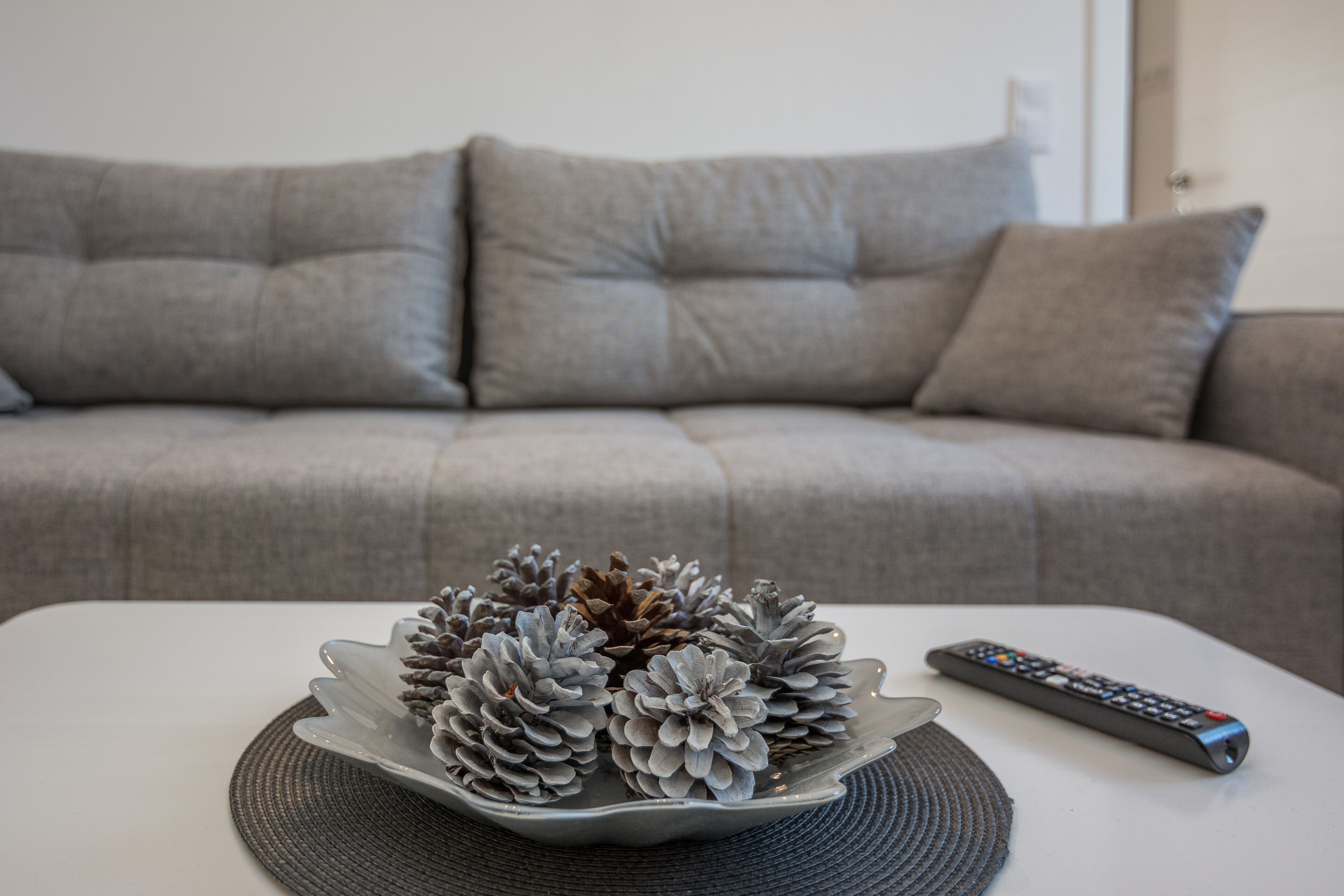 A white table with a decorative pine cone arrangement and a remote control.