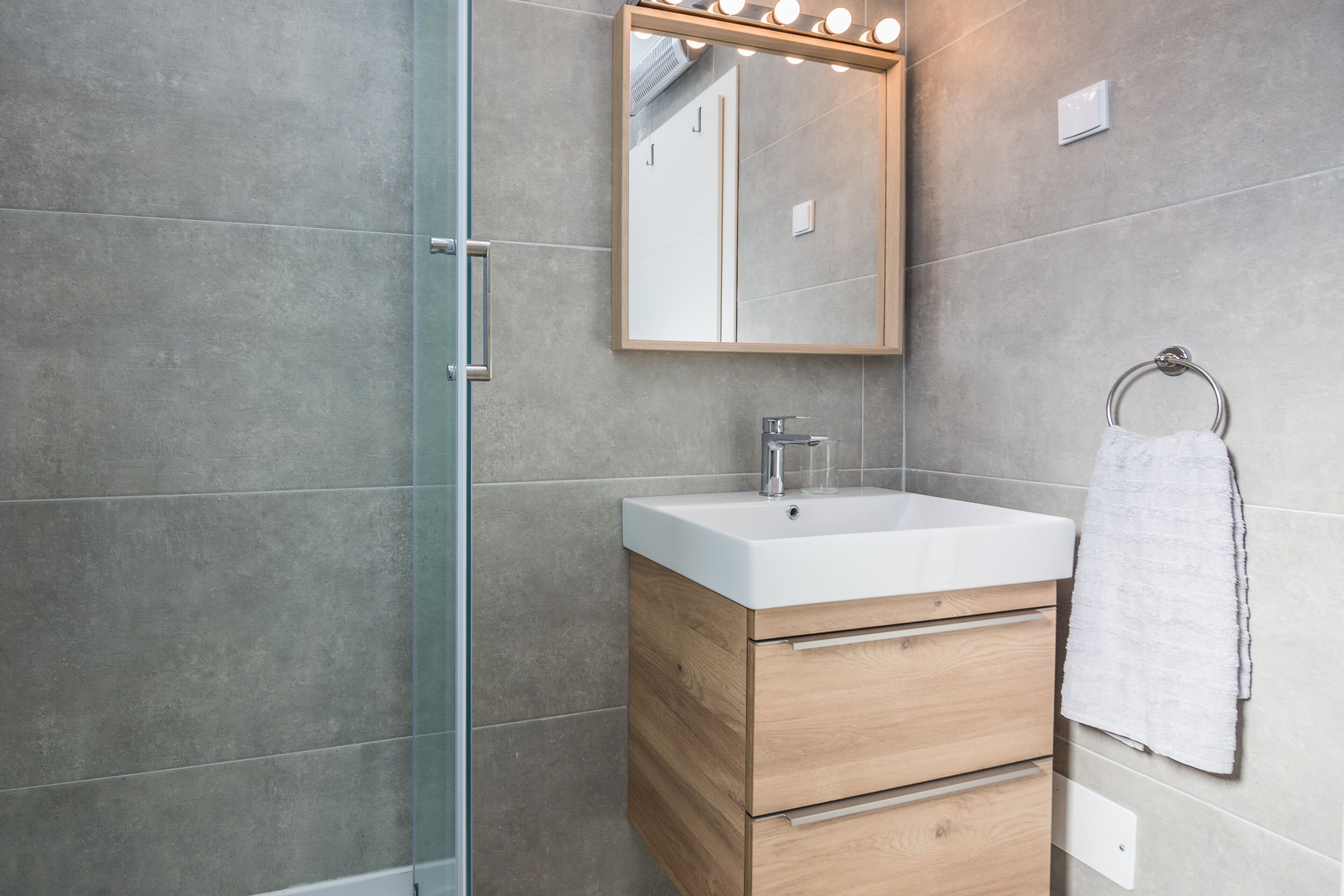 A modern bathroom with a glass shower enclosure, a wooden vanity with a white sink, and a mirror with lights.