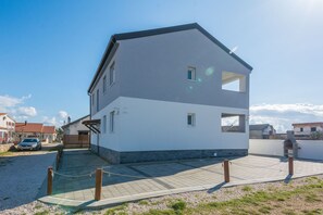 A two-story house with a large front porch and a driveway leading to a parked car. - Apartments Pejakovic (Vir)