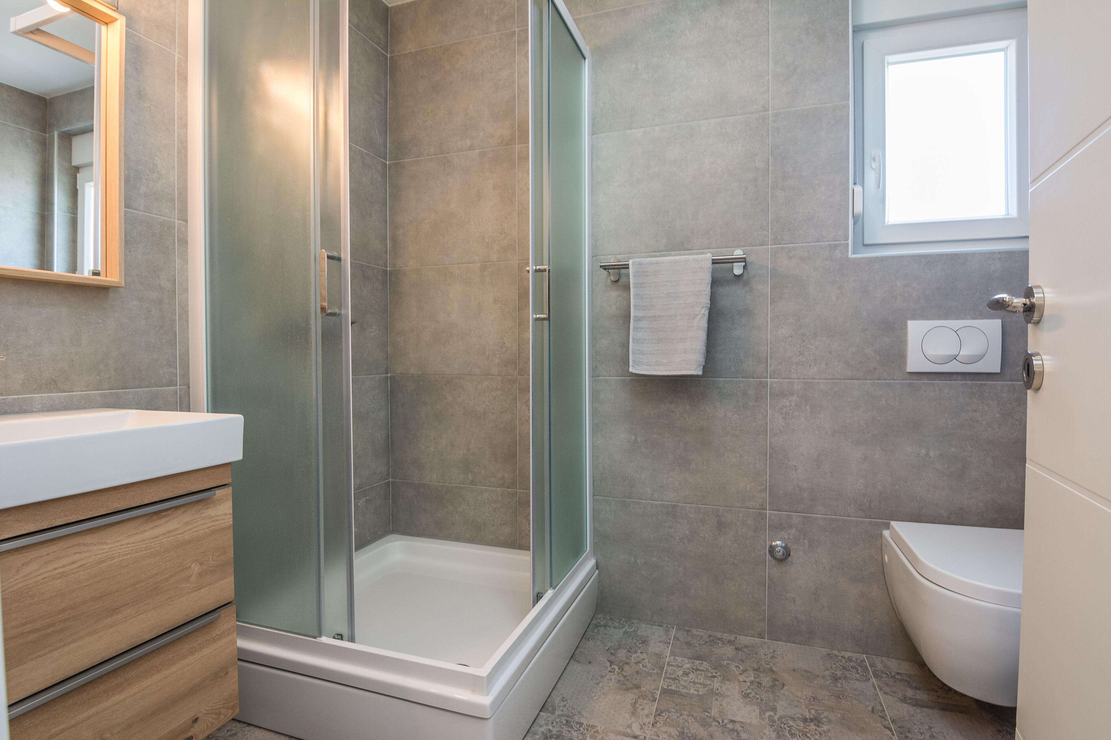 Un baño moderno con ducha envuelta en vidrio, tocador de madera y lavamanos blanco.