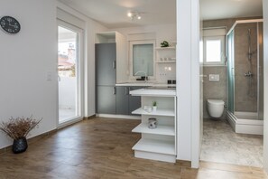 A modern kitchen with white cabinetry, a built-in oven, and a window with blinds. - Apartments Pejakovic (Vir)
