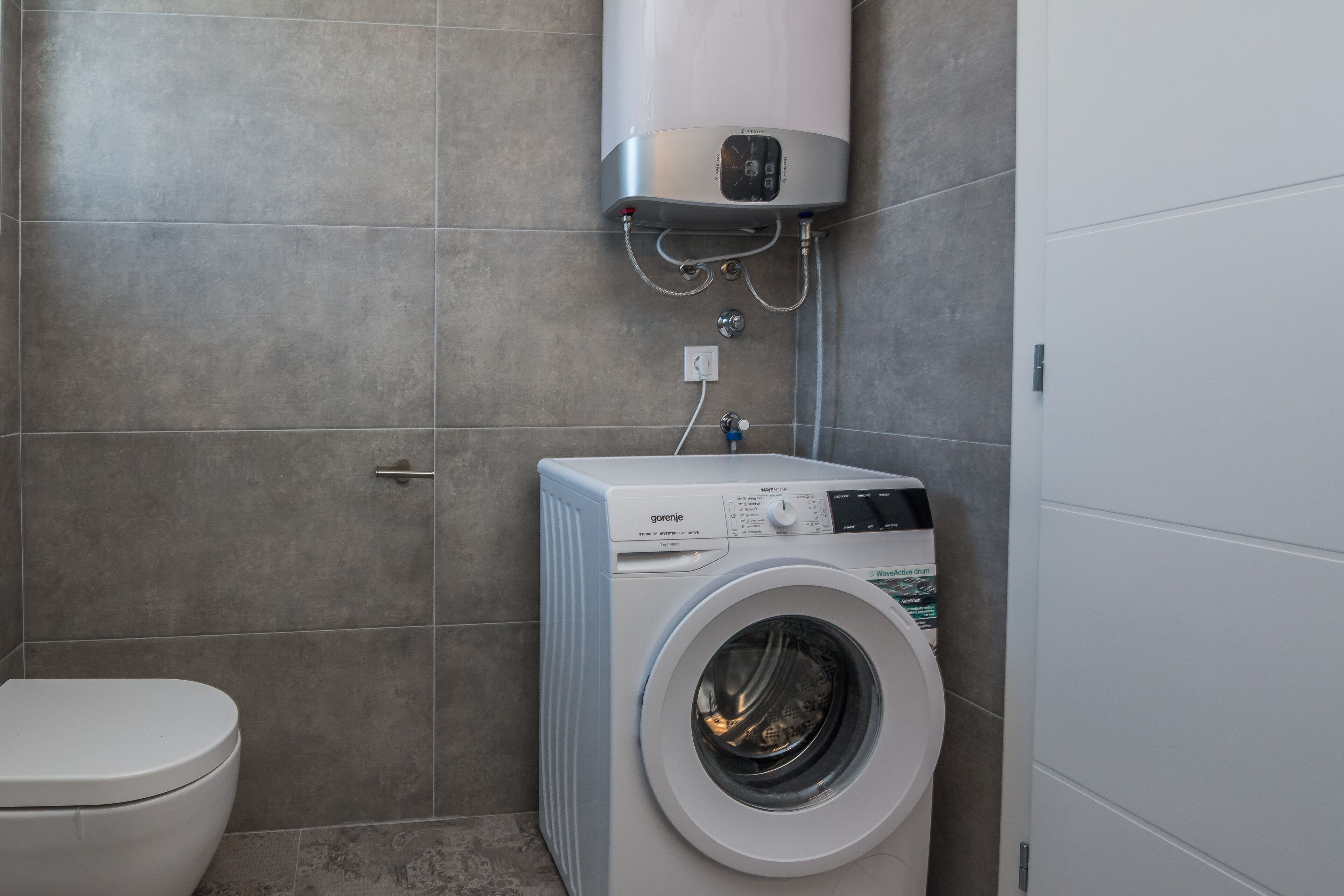 Une petite salle de bain équipée d’un lave-linge, de toilettes et d’un chauffe-eau.