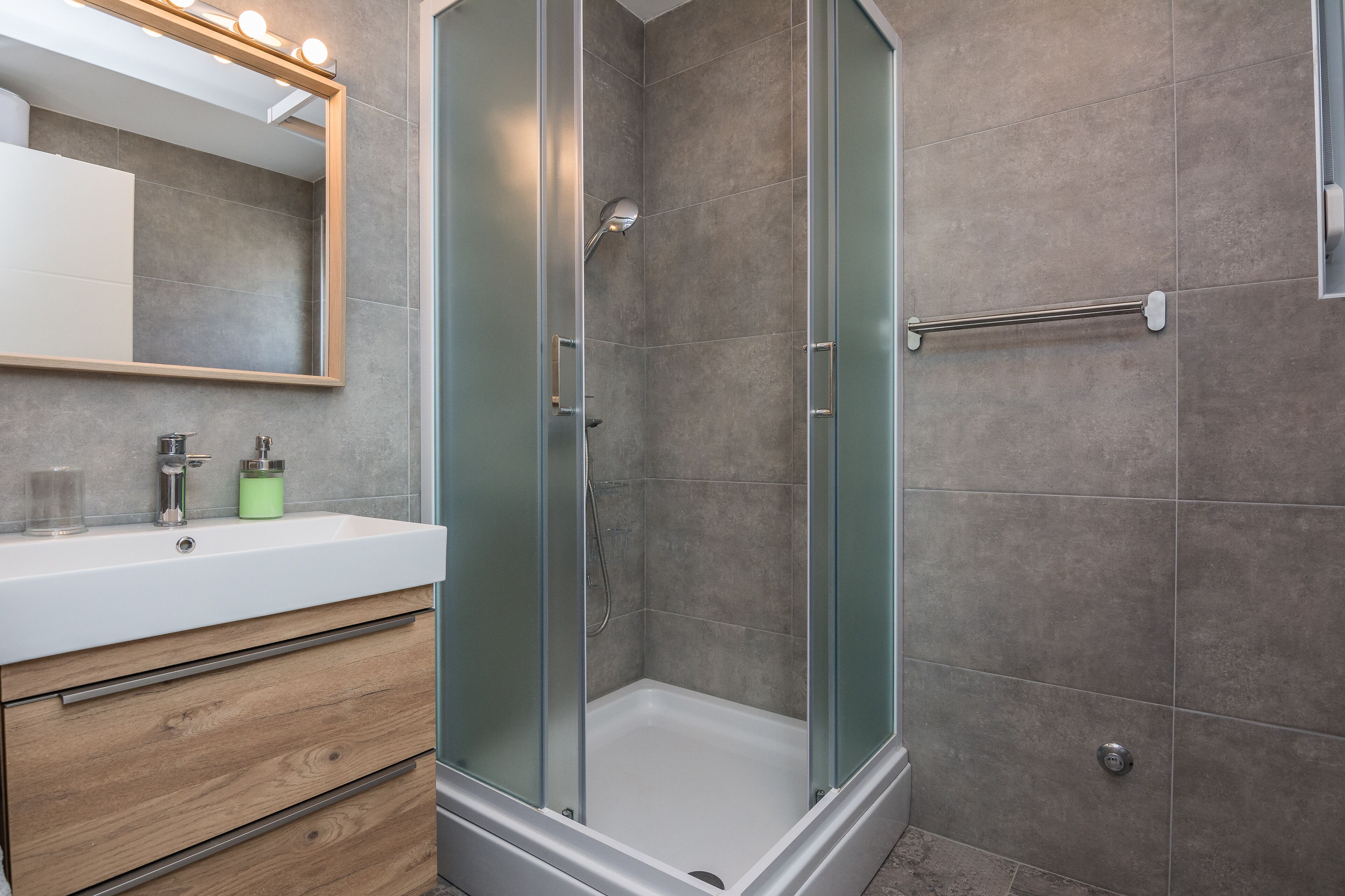 A modern bathroom with a glass-enclosed shower, a vanity with a mirror, and a towel rack.