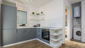 A modern kitchen with grey cabinets, a built-in oven, and a washing machine. - Apartments Pejakovic (Vir)