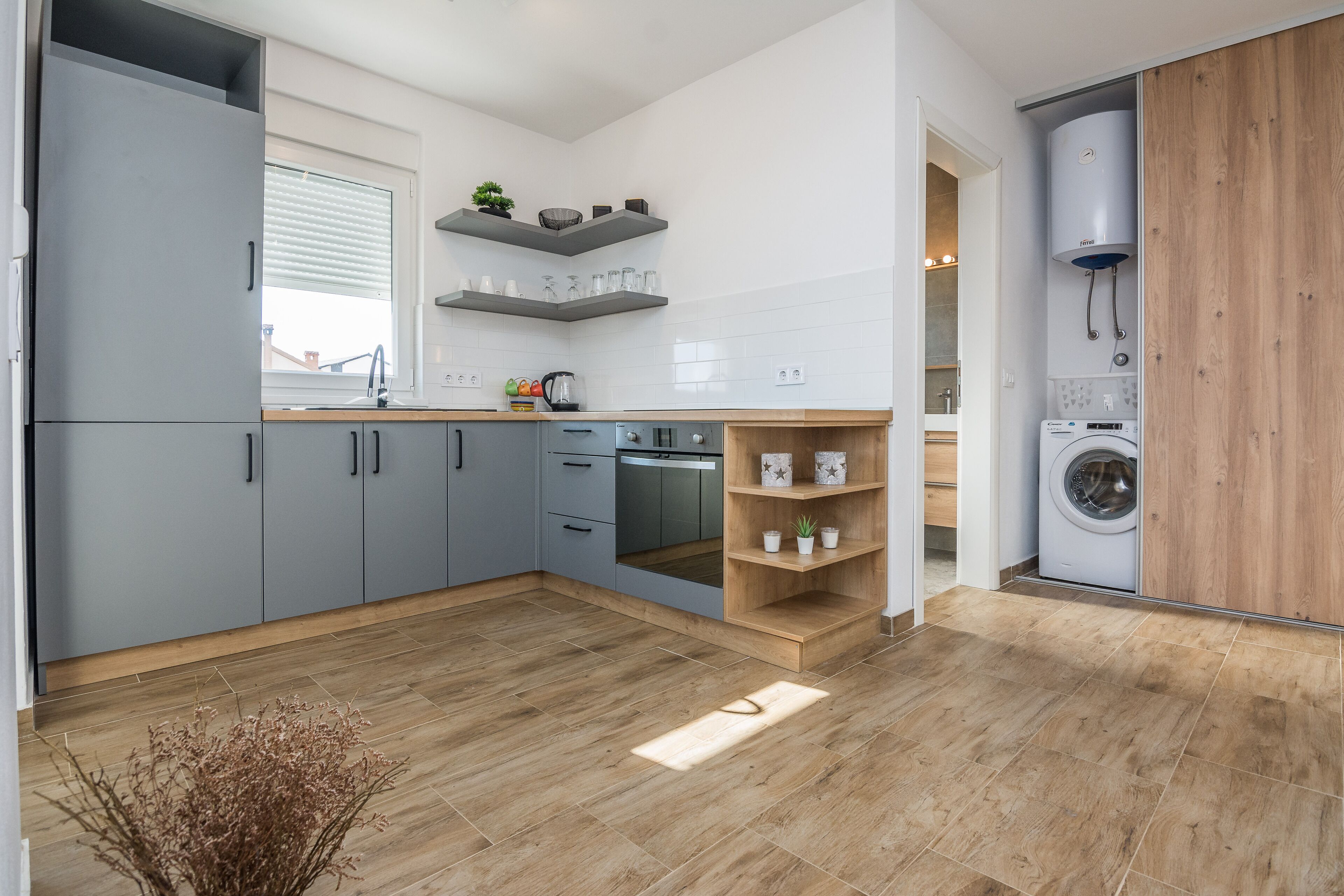 A modern kitchen with grey cabinets, a built-in oven, and a washing machine in the corner.