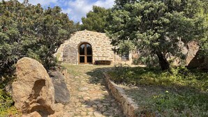 Un edificio de piedra con un arco central, rodeado de árboles y un sendero de piedra que conduce hacia él.