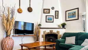 Ein Wohnzimmer mit einem grünen Sofa, einem Holztisch, einem Fernseher, einem Kamin und verschiedenen Wanddekorationen.