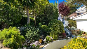 Ein üppiger Garten mit verschiedener Pflanzen- und Blumenpracht, einer Steinmauer und einer Treppe, die zu einem Gebäude führt.