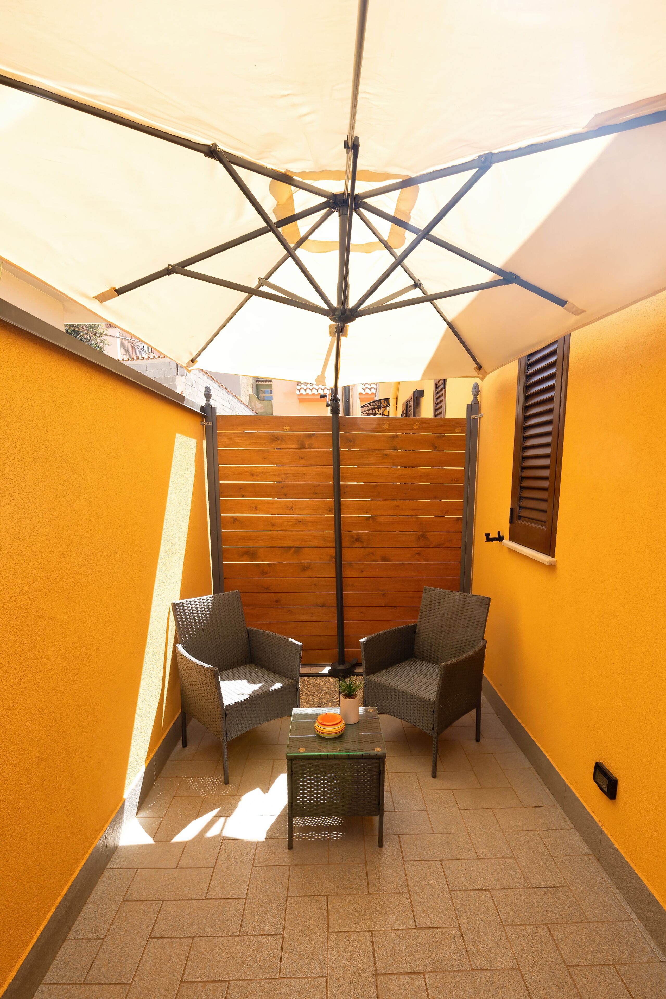 A small patio area with two wicker chairs, a glass table, and a wooden fence.