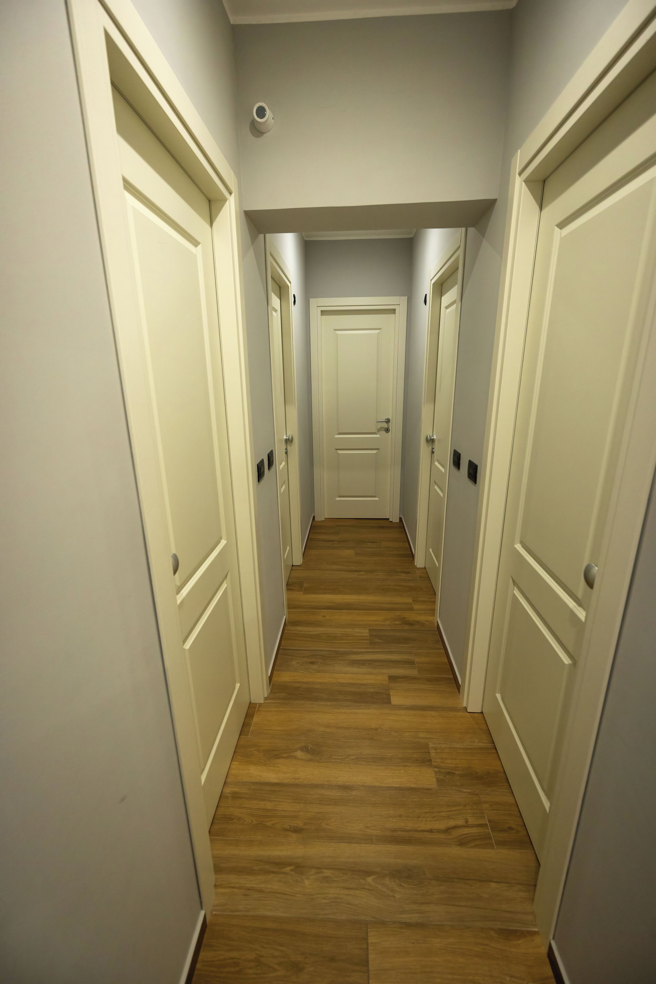 Un corridoio stretto con pavimento in legno e porte bianche su entrambi i lati.