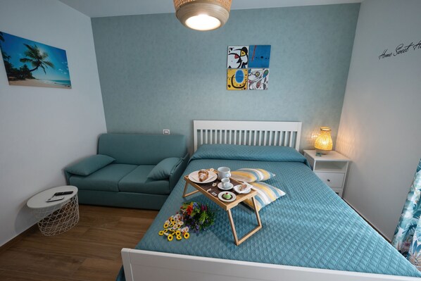 A bedroom with a bed, a bedside table with a lamp, a small round table with a tray of breakfast, a sofa, and a painting on the wall. - Sunset House Balestrate (Balestrate)