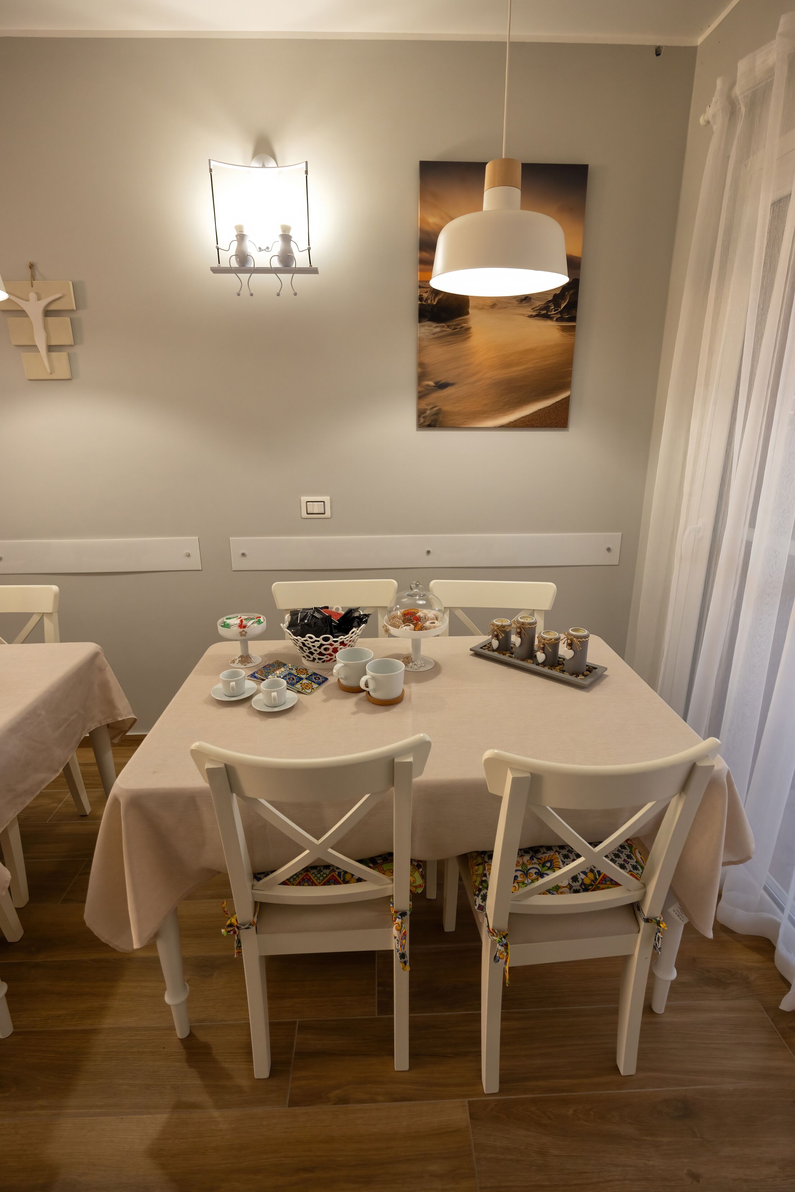 A dining area with a table set for four, white chairs, a pendant light, and a wall-mounted light fixture.