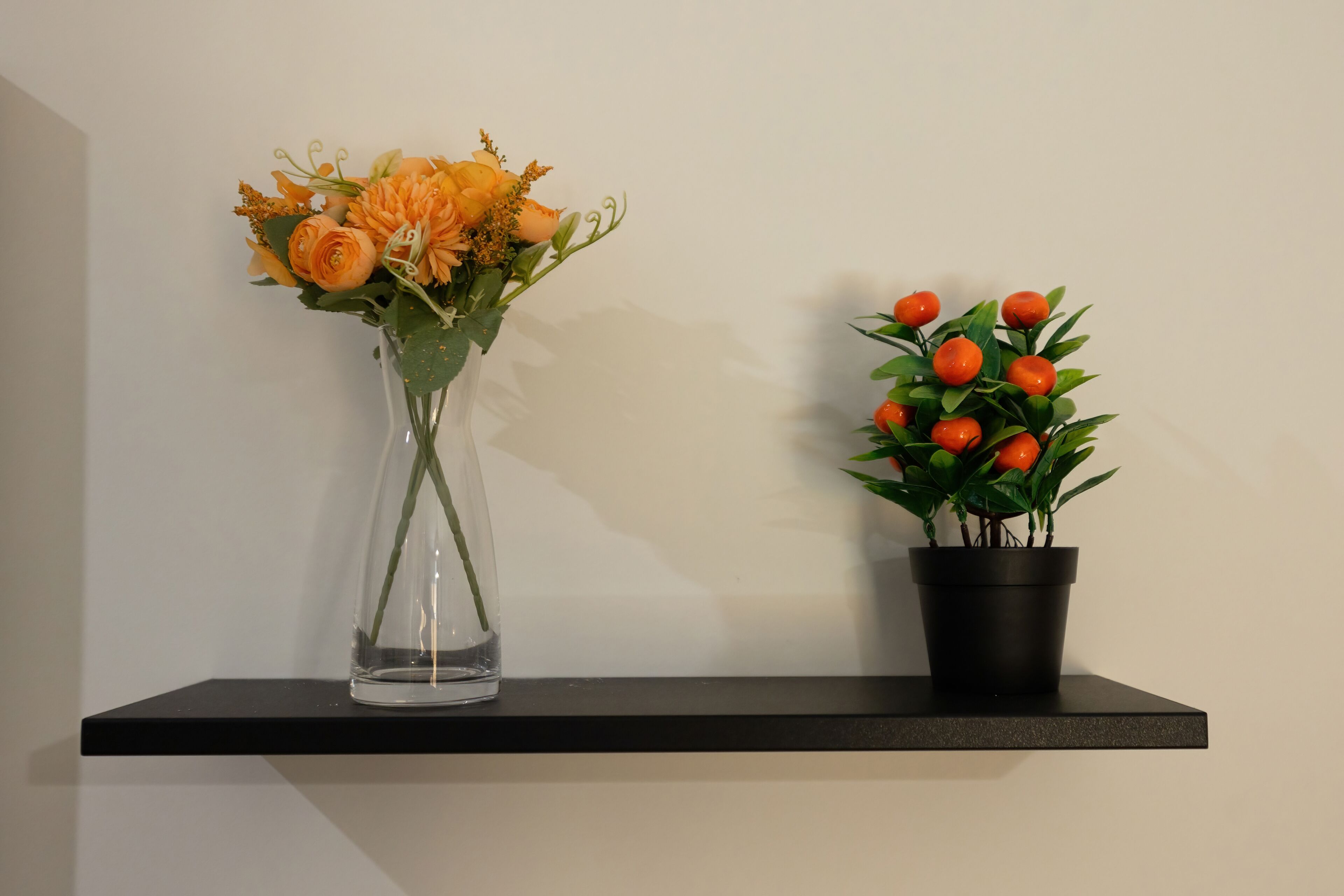 A clear vase with flowers and a potted plant on a shelf.