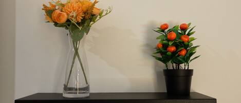 A clear vase with flowers and a potted plant on a shelf.