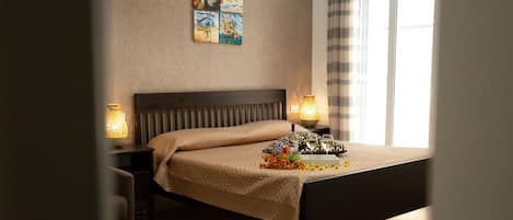A neatly made bed with a headboard, two bedside tables with lamps, a wall-mounted painting, and a large window with curtains.