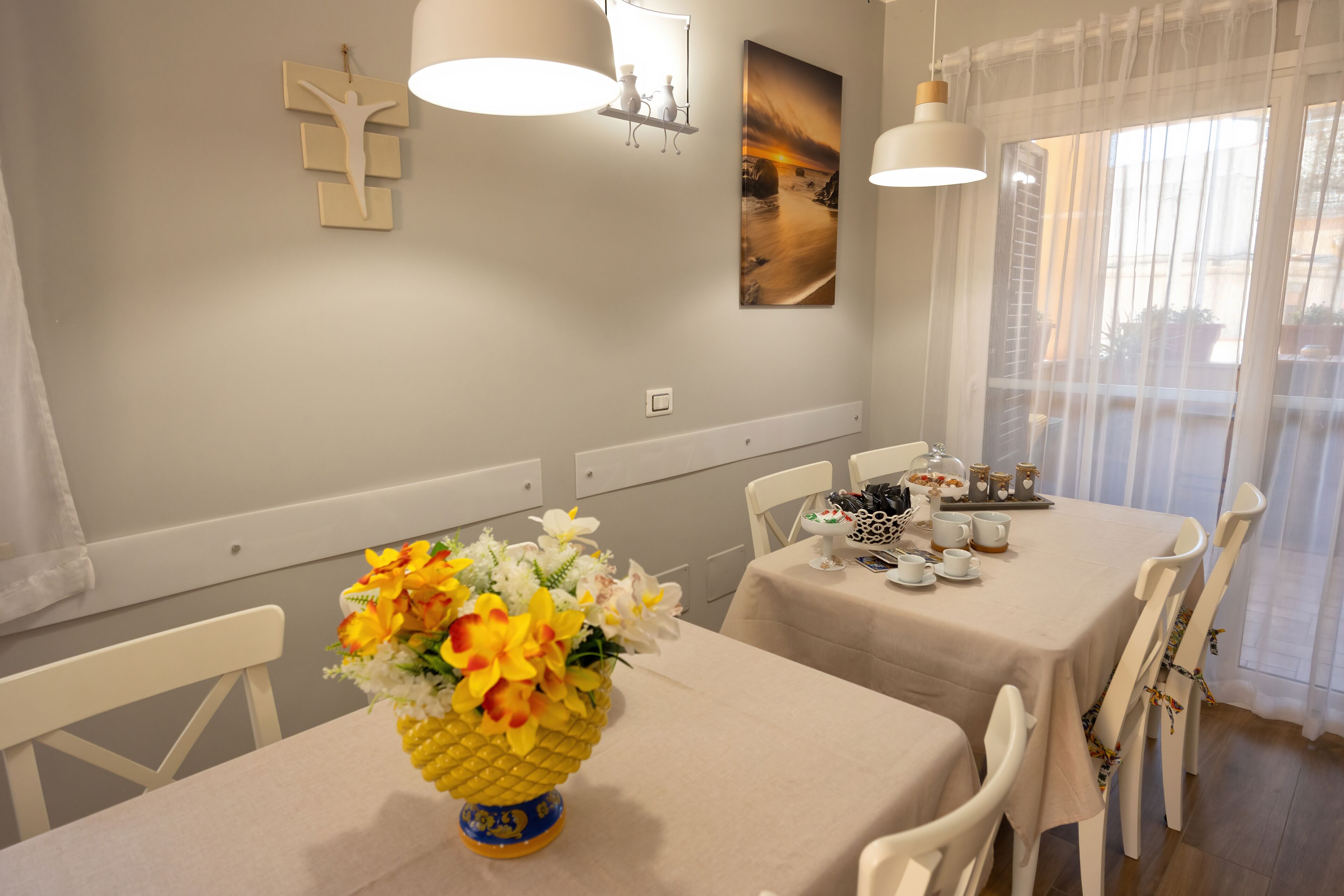 A dining area with a table set for two, a vase of flowers, and a painting on the wall.