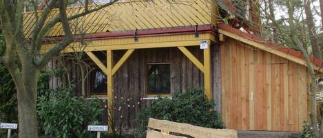 A rustic wooden building with a yellow roof, a wooden bench in front, and a paved walkway.