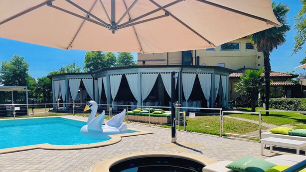 Una piscina con un flotador con forma de cisne, un jacuzzi y una zona de estar cubierta con vistas a un edificio.
