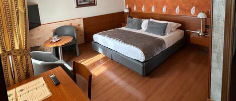 A hotel room with a bed, a desk, a chair, a ceiling fan, and a wall with a leaf pattern.