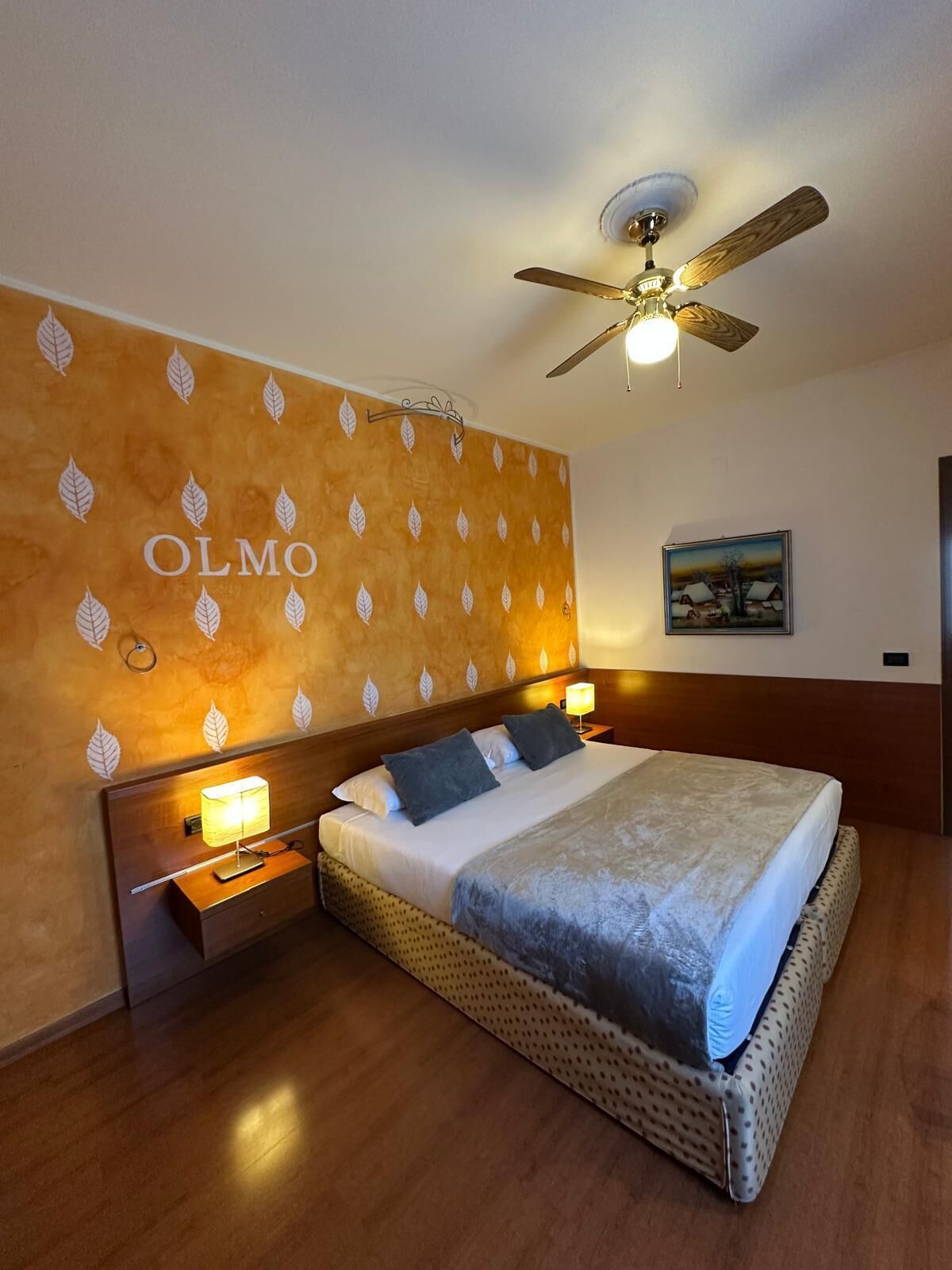 Una habitación de hotel con una cama, un ventilador de techo, una pared con motivos de hojas y un cuadro.