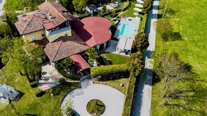 Vista aérea de una propiedad residencial con piscina, un camino circular y un edificio de techo rojo.