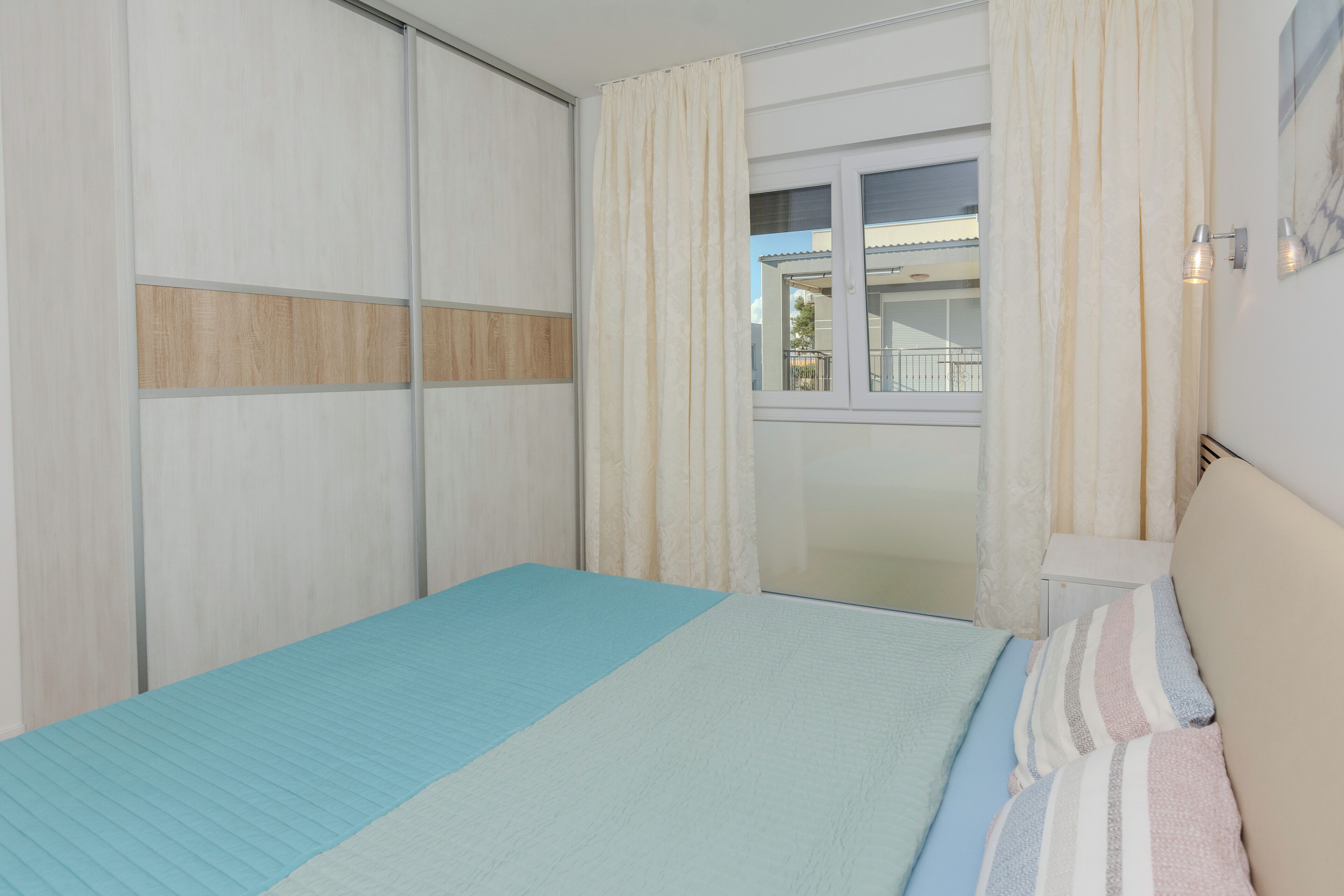 A bedroom with a bed, curtains, a window, and a nightstand.