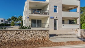Un edificio moderno de varios pisos con balcones, un muro de piedra en primer plano y un cielo azul despejado.