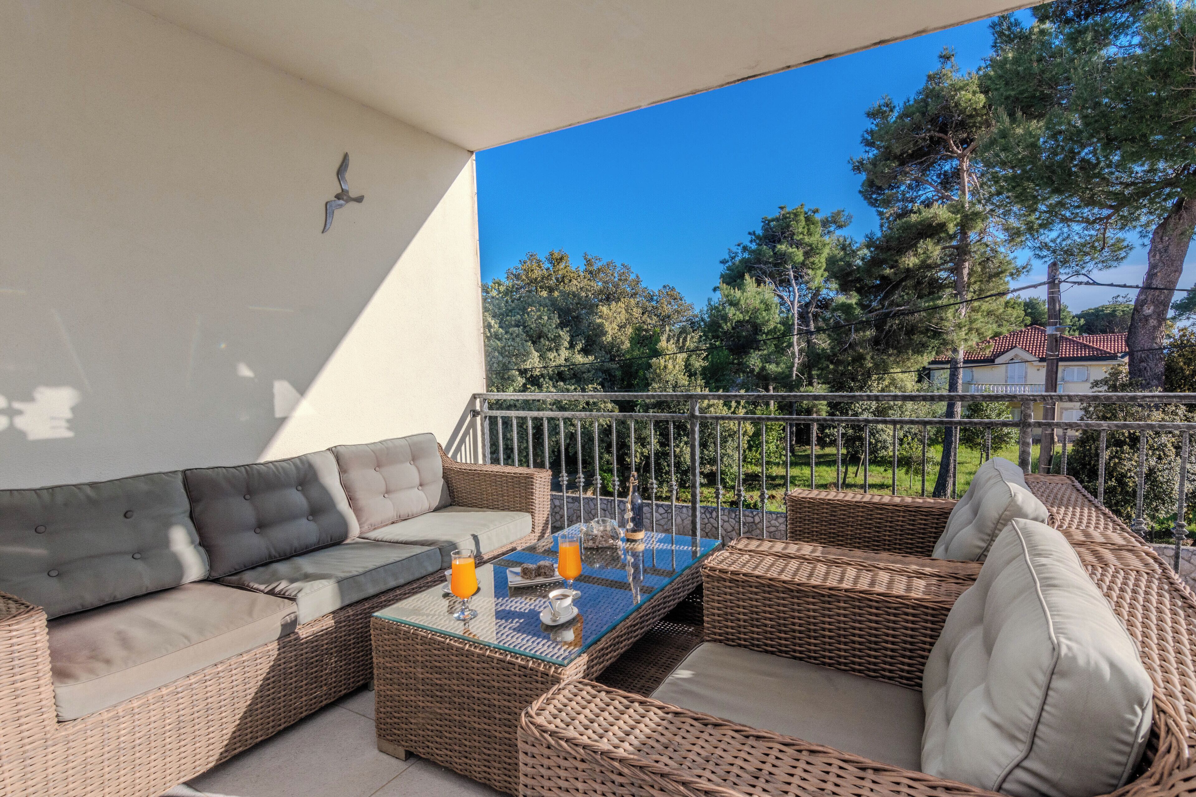A balcony with wicker furniture, including a sofa and chairs, and a glass table with drinks.