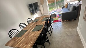 Ein Essbereich mit einem Holztisch und schwarzen Stühlen, einem grauen Sofa und Blick auf einen Garten durch große Fenster.