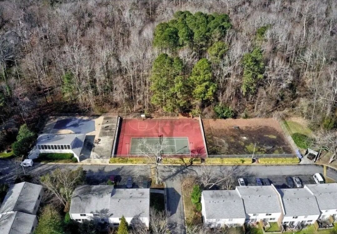Vista aérea de una zona residencial con una cancha de baloncesto, casas y un área boscosa.