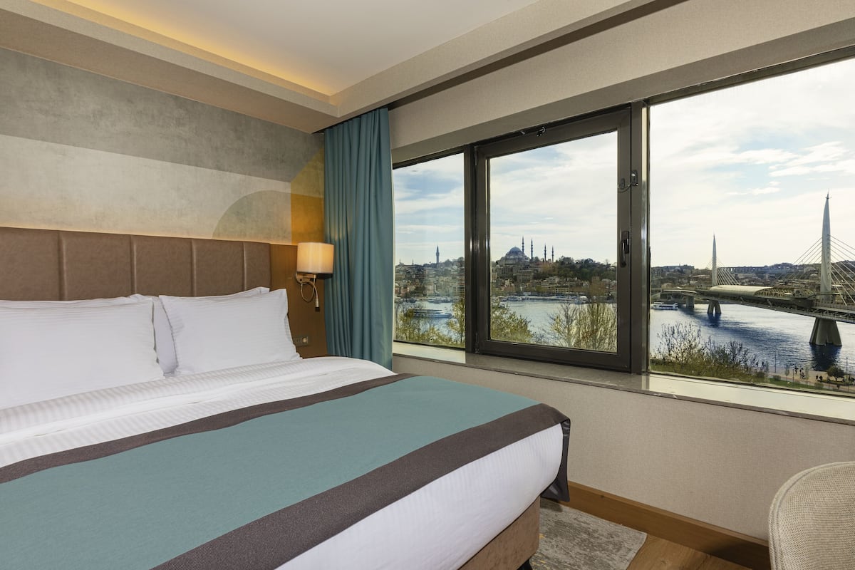 A hotel room with a large bed, a view of a bridge, and a cityscape.