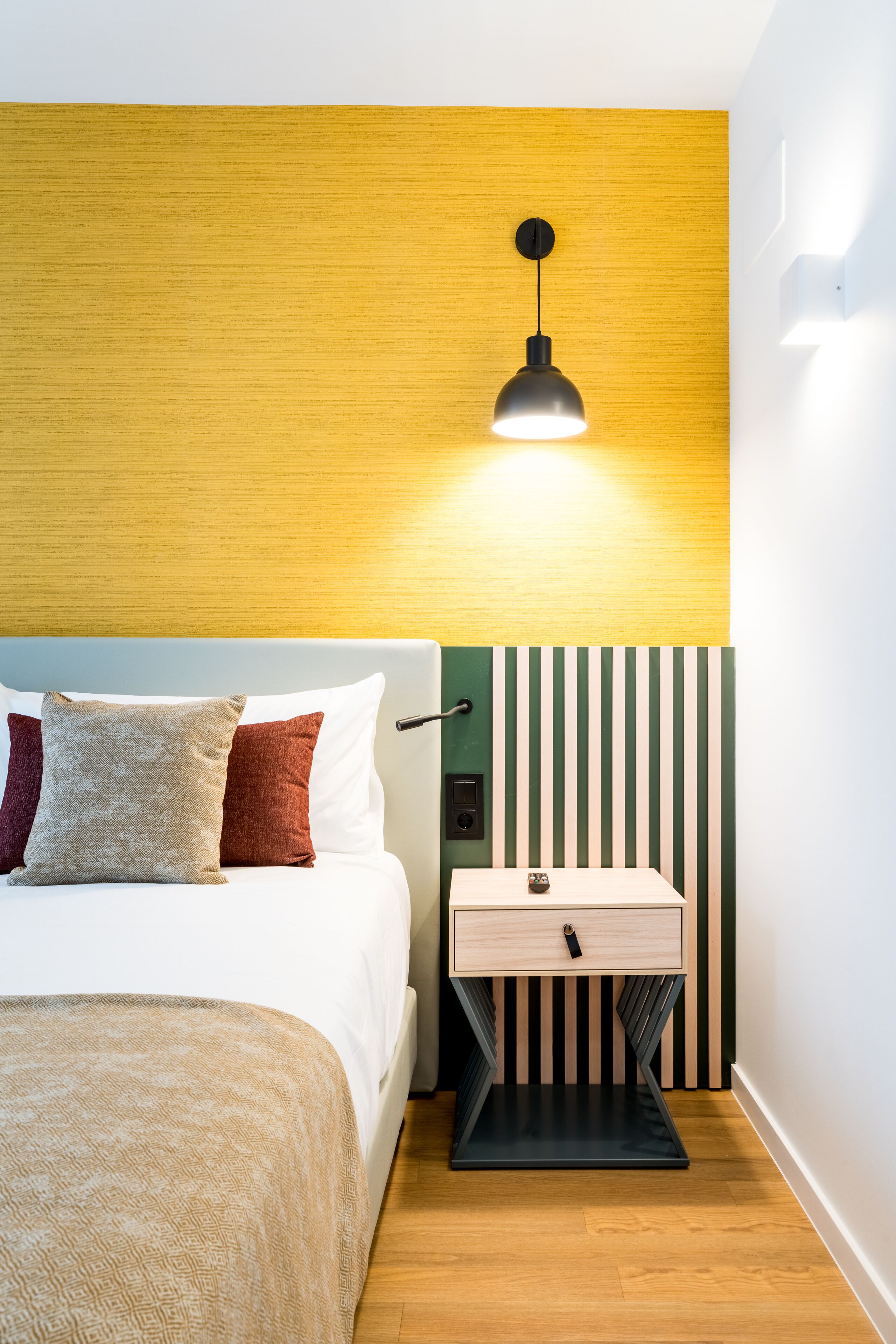 A neatly arranged bedroom with a bed, bedside table, and a wall-mounted lamp.