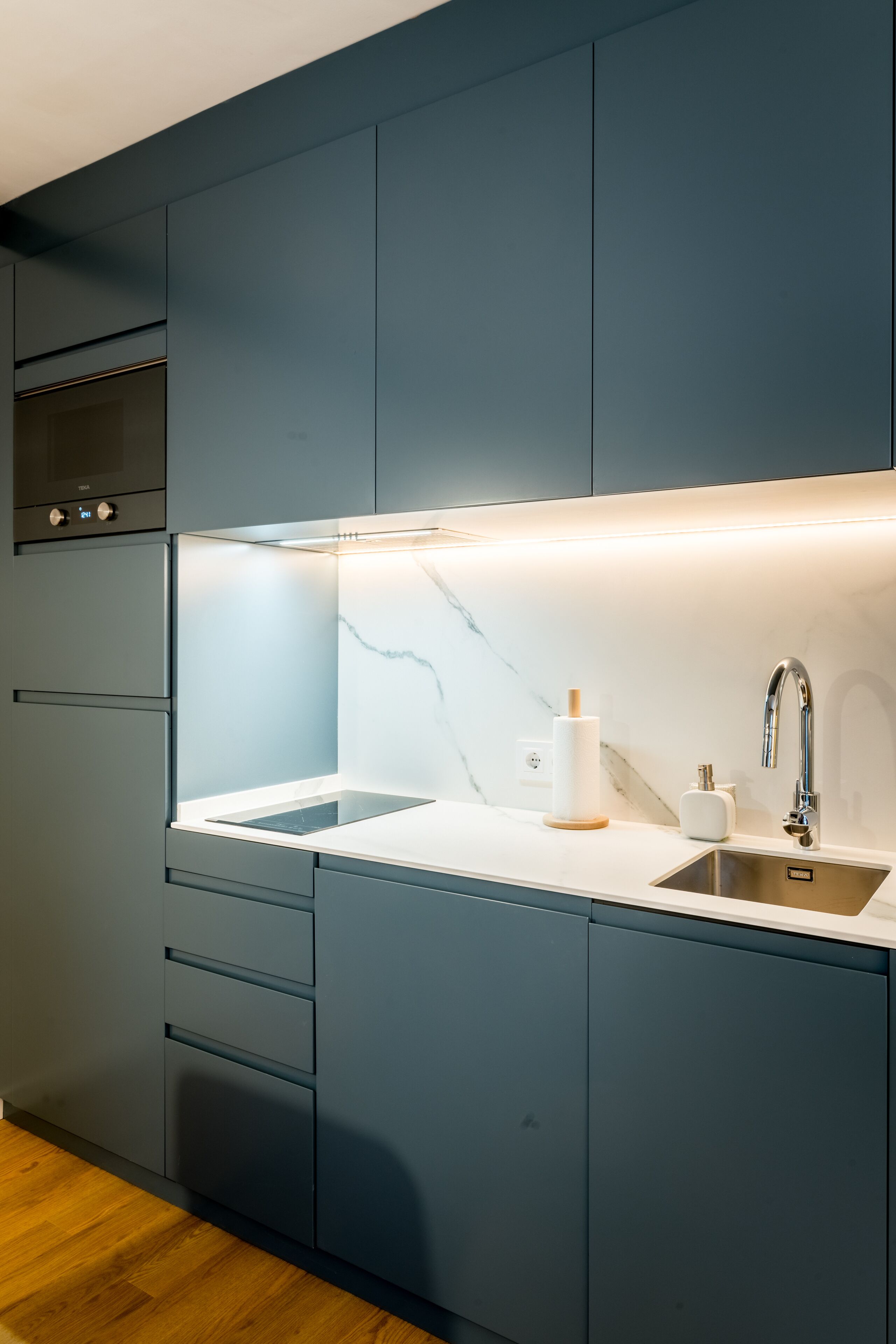 Una cocina moderna con armarios oscuros, encimera de mármol y horno empotrado.
