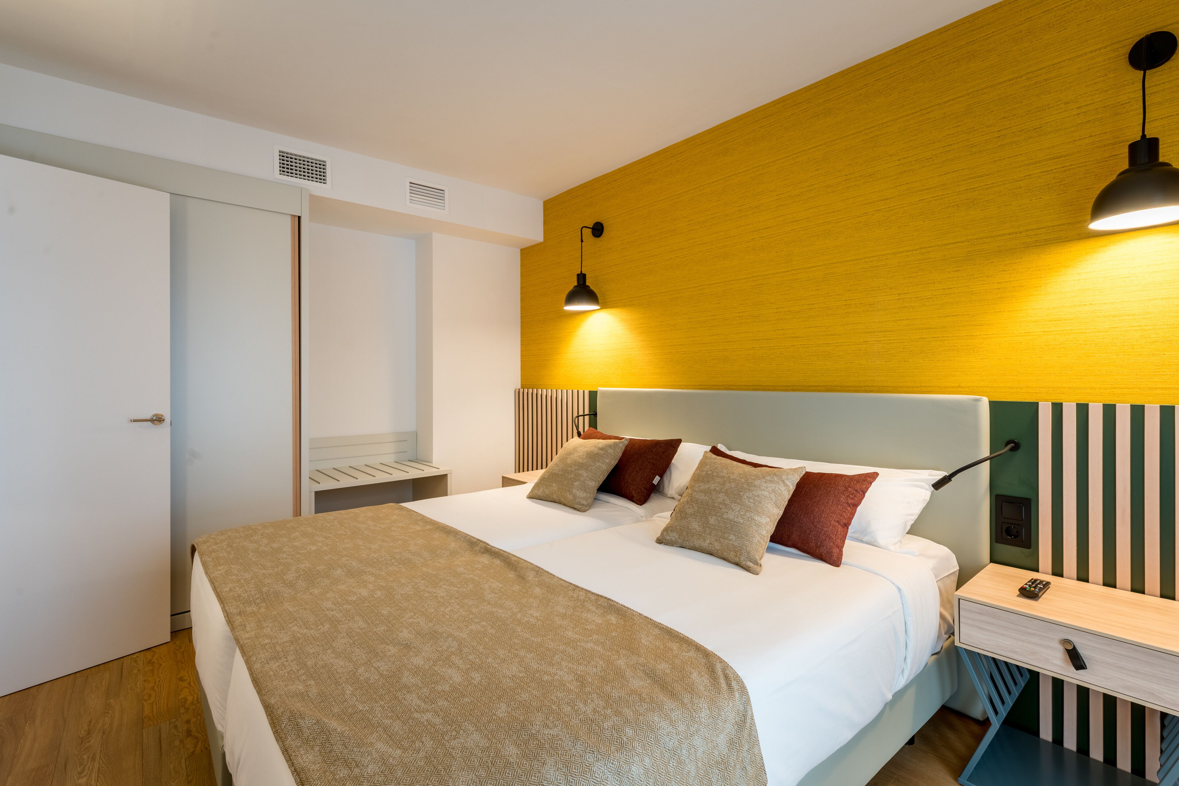 A modern hotel room with a large bed, a bedside table with a lamp, and a wardrobe.