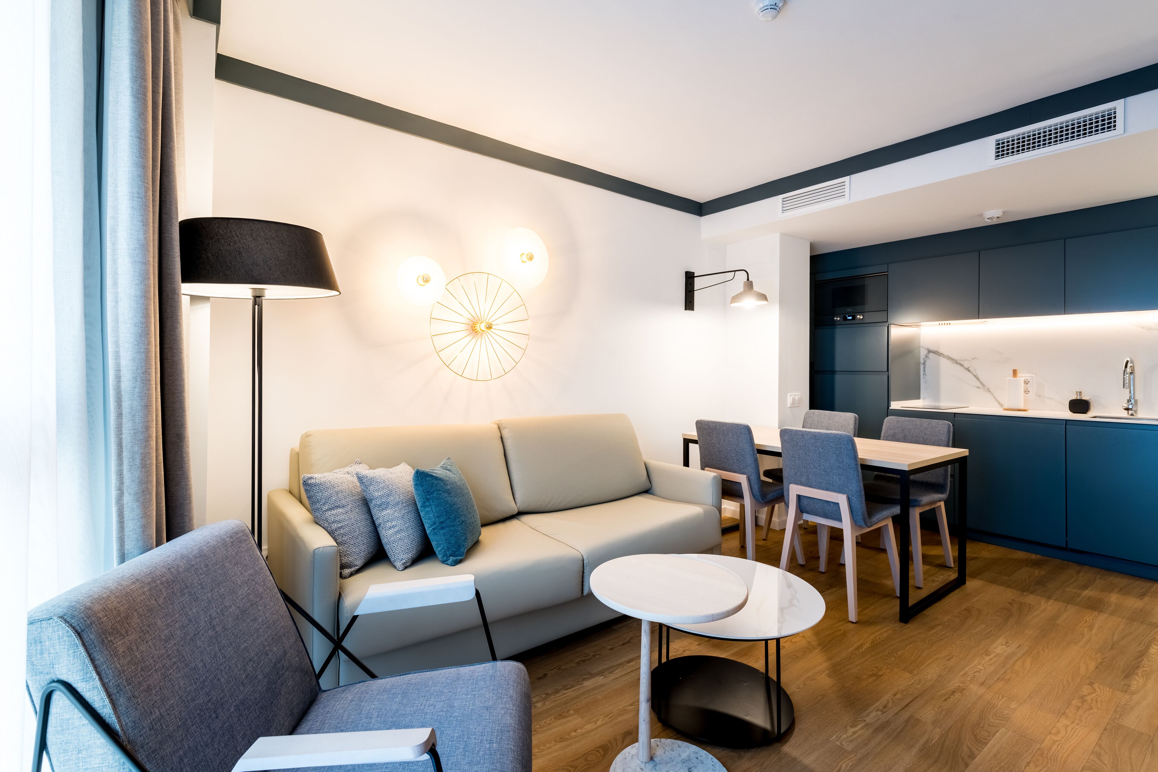 A modern living room with a sofa, chairs, a small table, and a kitchen area with a counter and cabinets.